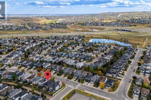 Aerial view of a neighborhood with many houses, a pond, and distant city skyline and highway overpasses. - 304 Evanston View Nw, Calgary