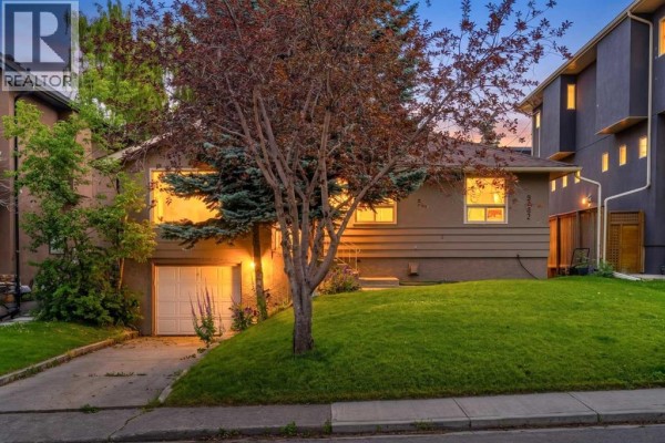 Front view of a house with a sloped lawn, trees, and a detached garage. - 3042 28 Street Sw, Calgary