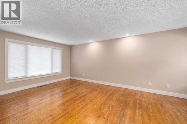 Living room with hardwood floors, beige walls, recessed lighting, and a large window. - 3042 28 Street Sw, Calgary