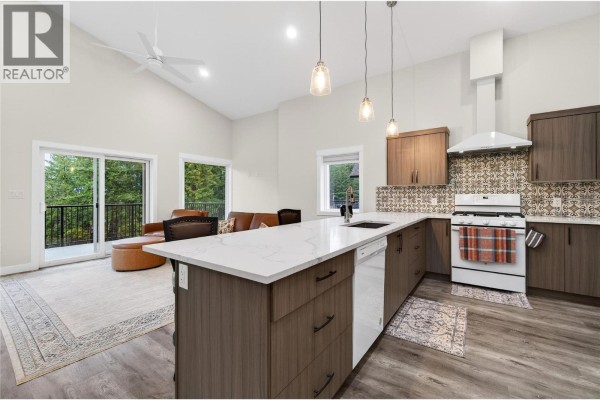Open concept kitchen and living room with large island, modern cabinets, vaulted ceiling, and sliding glass doors. - 3044 Cedar Drive, Blind Bay