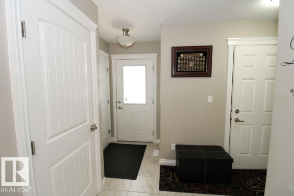 Interior entryway with white doors, tiled floor, and a dark storage ottoman. - 3048 Harvey Cr Nw, Edmonton