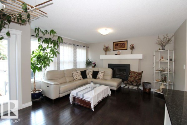 Living room with a sectional sofa, fireplace, dark wood floors, and large windows. - 3048 Harvey Cr Nw, Edmonton