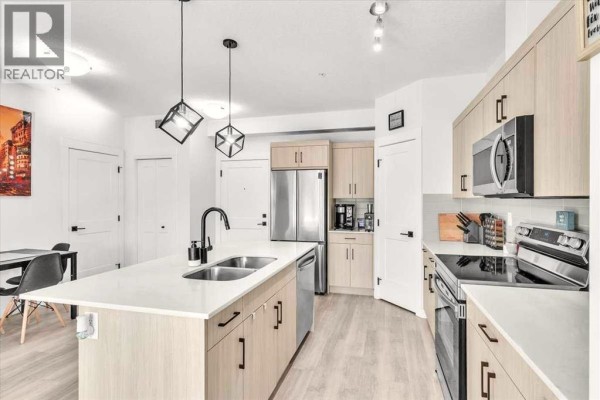 Open-concept kitchen and living area with a large island, stainless steel appliances, and light wood cabinetry. - 305, 30 Sage Hill  Nw, Calgary