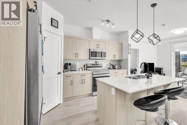 Kitchen and dining area featuring a large island, modern pendant lights, and stainless steel appliances. - 305, 30 Sage Hill  Nw, Calgary