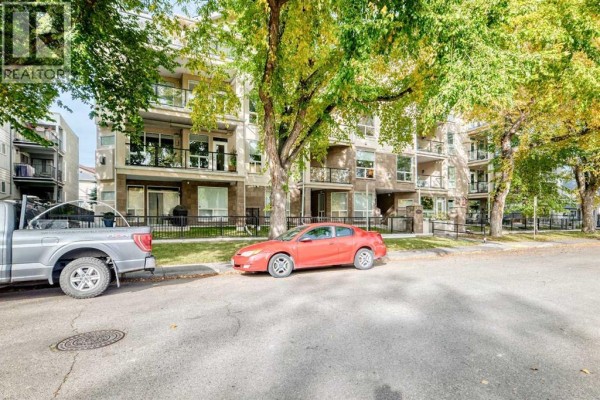 Street view of an apartment building with a red car and silver truck parked. - 305, 3412 Parkdale Boulevard Nw, Calgary