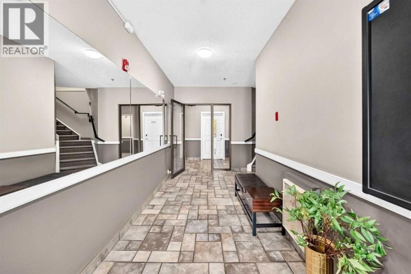 Interior hallway with tiled floors, mirrors, benches, stairs, and apartment doors. - 305, 3412 Parkdale Boulevard Nw, Calgary