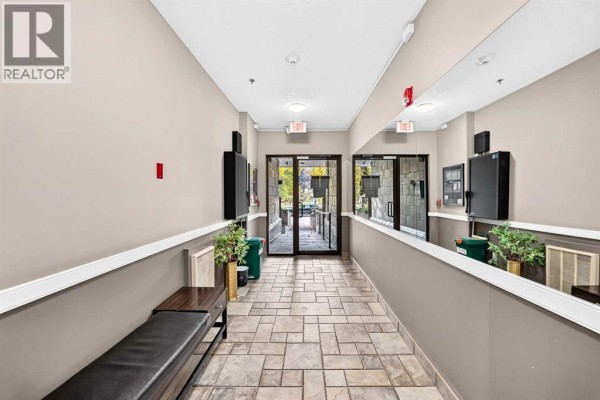 View down the interior hallway towards the building's glass entrance doors. - 305, 3412 Parkdale Boulevard Nw, Calgary