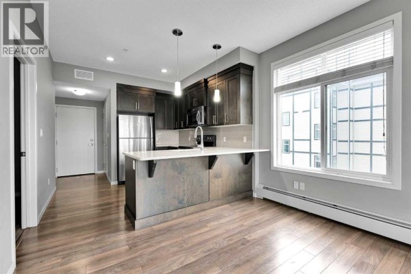 Kitchen with dark wood cabinets, stainless steel appliances, and island. - 305, 6703 New Brighton Avenue Se, Calgary