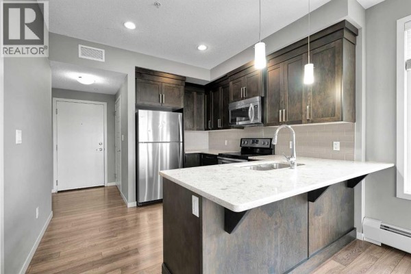 Kitchen featuring dark wood cabinets, island with white countertop, and stainless steel appliances. - 305, 6703 New Brighton Avenue Se, Calgary