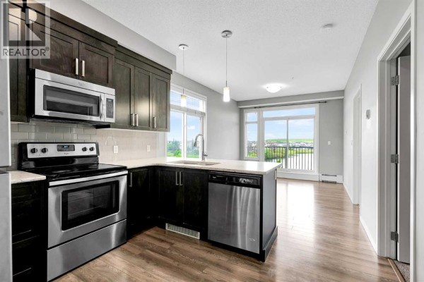 Kitchen with dark cabinets, stainless steel appliances, and view of dining area and balcony. - 305, 6703 New Brighton Avenue Se, Calgary