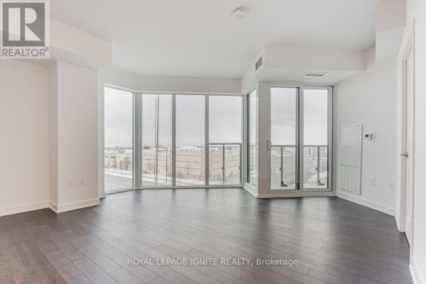 Bright living room with dark hardwood floors and a large bay window offering city views. - 305 - 100 Eagle Rock Way, Vaughan