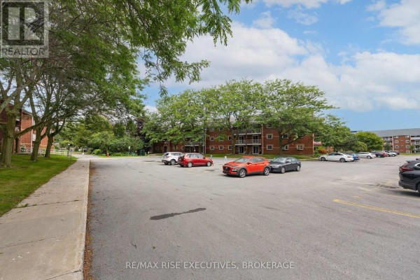 Parking lot with several cars parked, adjacent to a brick apartment building and trees. - 305 - 561 Armstrong Road, Kingston
