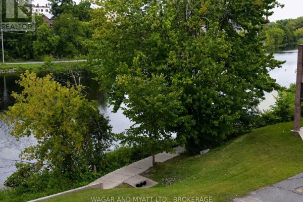 View from a balcony overlooking the water, trees, a parking lot, and a white SUV. - 305 - 9 Centre Street S, Greater Napanee