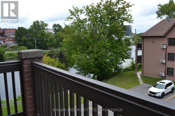 Living room with beige carpet and an open-concept kitchen with light wood cabinets. - 305 - 9 Centre Street S, Greater Napanee