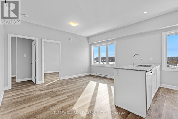 Empty bedroom with light grey walls, a large window, and wood-look flooring. - 305 - 979 North Russell Road, Russell