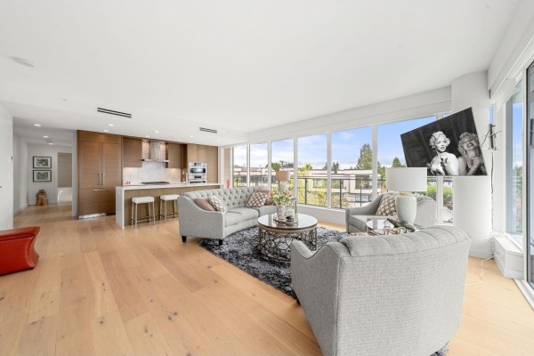Living room with light wood floors, grey sectional sofa, kitchen island, and large windows. - 305 1439 George Street, White Rock