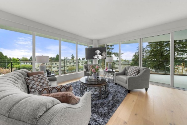 Living room with grey upholstered furniture, circular rug, decorative tables, and floor-to-ceiling windows. - 305 1439 George Street, White Rock