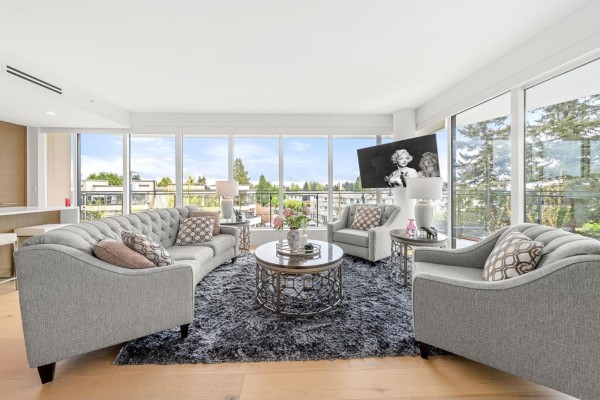 Bright living area with a curved sofa, armchair, circular rug, and wide windows overlooking trees. - 305 1439 George Street, White Rock