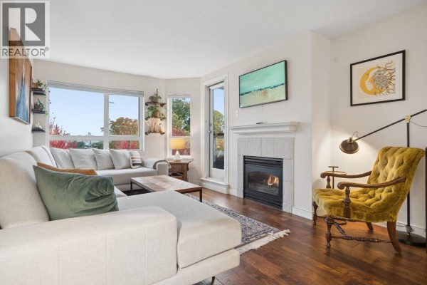 Living room with a sectional sofa, gas fireplace, and a large window overlooking trees. - 305 1707 Charles Street, Vancouver