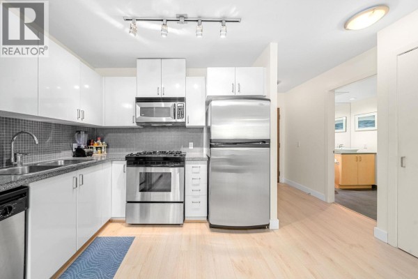 Kitchen with light wood floors, white cabinets, stainless steel appliances, and view of bathroom. - 305 175 W 1st Street, North Vancouver
