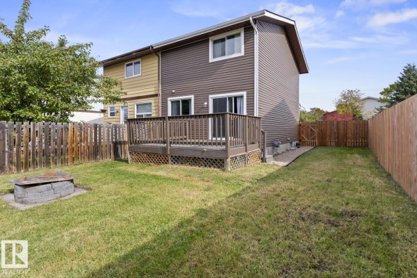 Backyard of the duplex with a wooden deck, fire pit, and wooden fence. - 305 19 St, Cold Lake
