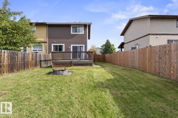 View of the fenced backyard with a wooden deck and a fire pit. - 305 19 St, Cold Lake
