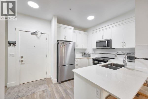 Interior view of an apartment entrance and a U-shaped kitchen with appliances. - 305 22577 Royal Crescent, Maple Ridge