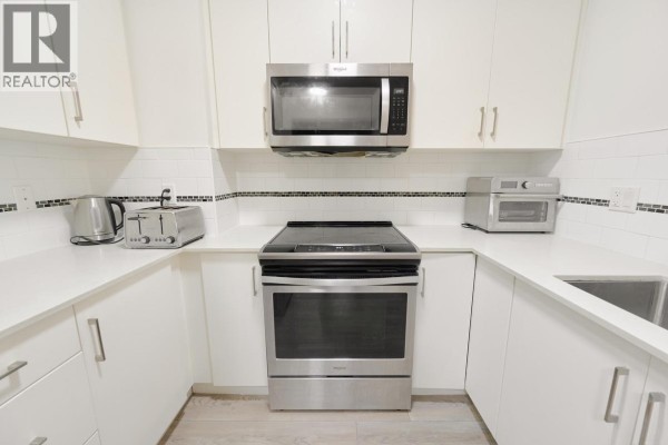 Close-up of a U-shaped kitchen with white countertops, backsplash, and appliances. - 305 22577 Royal Crescent, Maple Ridge