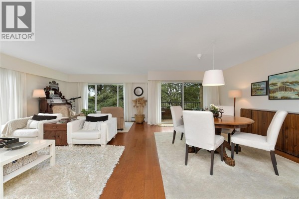 Living and dining area with white chairs, round table, and wood buffet against wall. - 305 2930 Cook St, Victoria