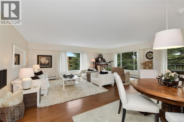 Living area with large windows, fireplace, white sofas, and a dining table. - 305 2930 Cook St, Victoria