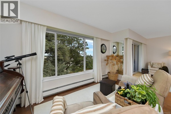 Living room with large window overlooking trees and water, telescope, and beige armchairs. - 305 2930 Cook St, Victoria