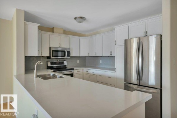 Corner kitchen with white cabinets, quartz countertops, stainless steel appliances, and a double sink. - #305 7839 96 St Nw, Edmonton