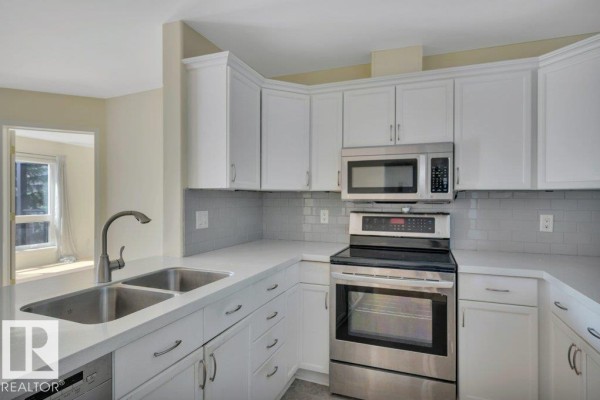View of the kitchen sink, white cabinets, stainless steel oven, and tiled backsplash. - #305 7839 96 St Nw, Edmonton