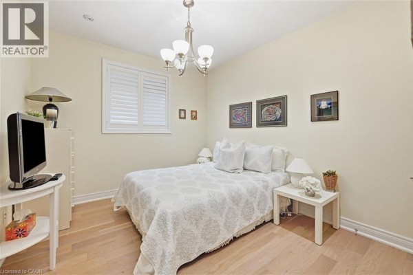 Bedroom with a queen-size bed, white bedding, and light wood floor. - 305 Caledon Avenue, Hamilton