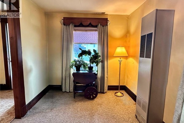 Carpeted living room with window, lamp, heater, and antique table - 305 North Cayuga Street W Dunnville