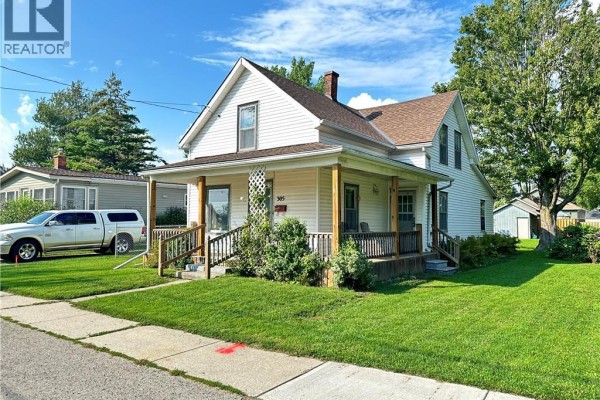 Side exterior view of white house with covered porch, driveway, and trees. - 305 North Cayuga Street W, Dunnville