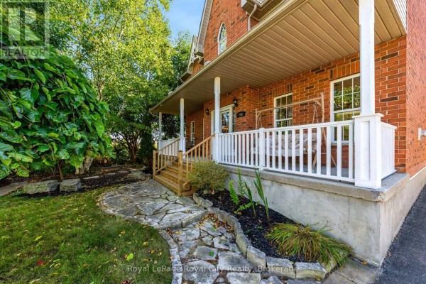 Close-up of a covered porch with white railings, a porch swing, and brick exterior. - 305 Ridge Road, Guelph/eramosa