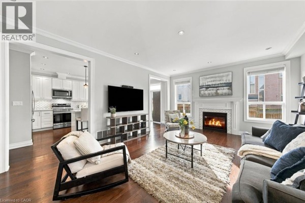 Living room with a fireplace, large television, sectional sofa, and hardwood floors, open to the kitchen. - 3053 Jenn Avenue, Burlington