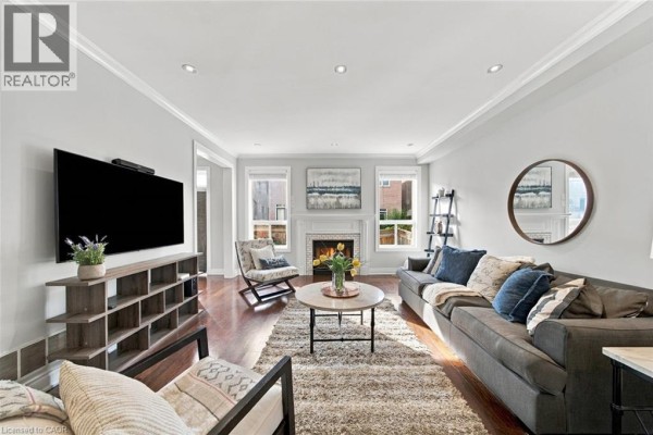 Living room showing a gas fireplace with a brick surround, sofa, and large rug on hardwood floors. - 3053 Jenn Avenue, Burlington