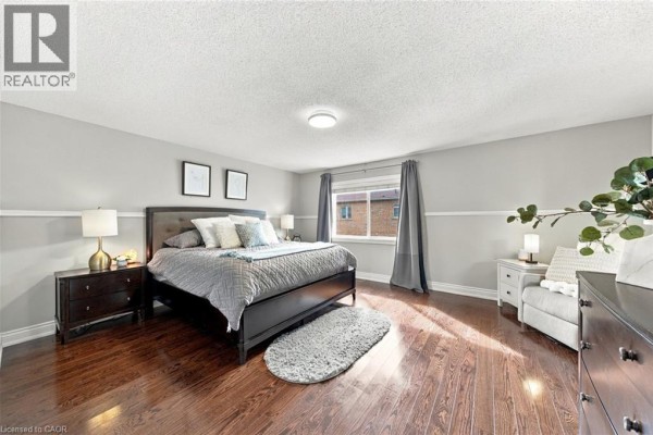 Primary bedroom with a king-sized bed, dark wood furniture, and hardwood floors overlooking a window. - 3053 Jenn Avenue, Burlington