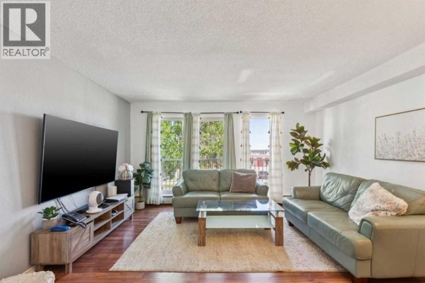 Living room with a large television, entertainment unit, two green sofas, glass coffee table, and balcony view. - 306, 1113 37 Street Sw, Calgary