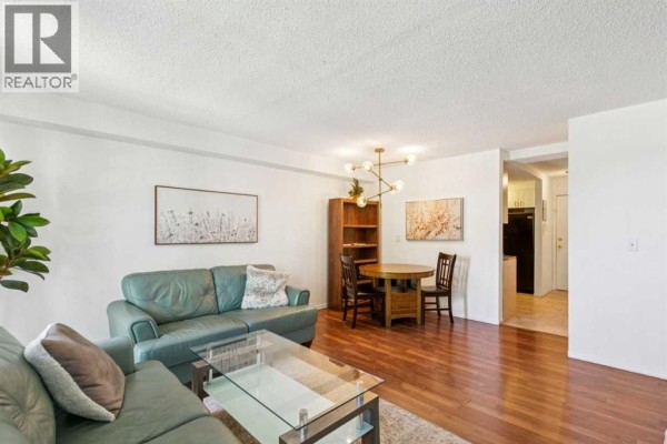 Living area showing sofas, dining table, bookshelf, and entrance to the kitchen. - 306, 1113 37 Street Sw, Calgary