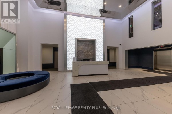 Apartment building lobby with white marble floors, a front desk, and a blue circular bench. - 306 - 16 Concord Place, Grimsby