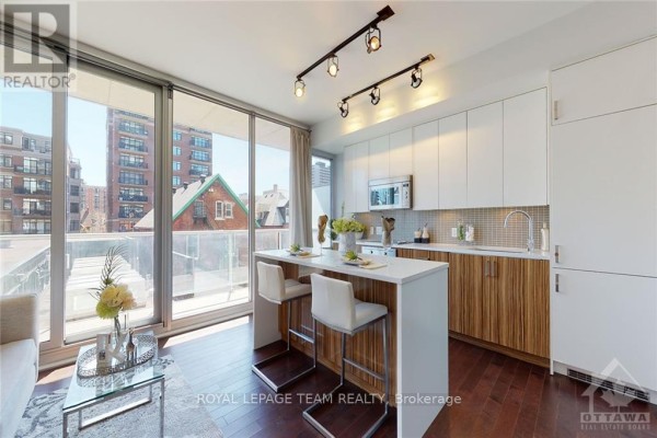 Kitchen island with bar stools and white cabinetry, overlooking the living area. - 306 - 300 Lisgar Street, Ottawa