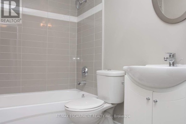 Compact bathroom with a white vanity, toilet, and a light grey tiled bathtub and shower. - 306 - 607 Heritage Drive, Waterloo