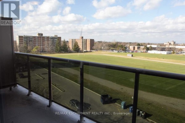 Balcony view of a green sports field and surrounding apartment buildings under a cloudy sky. - 306 - 607 Heritage Drive, Waterloo