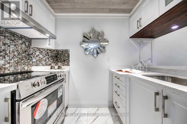 Small galley kitchen with white cabinets, stainless steel appliances, and a grey mosaic tile backsplash. - 306 - 7 Bishop Avenue, Toronto