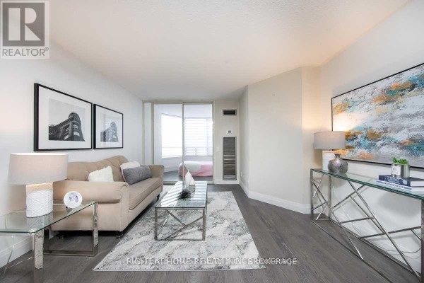 Living room with a beige sofa, glass coffee table, grey rug, and framed artwork on the wall. - 306 - 7 Bishop Avenue, Toronto