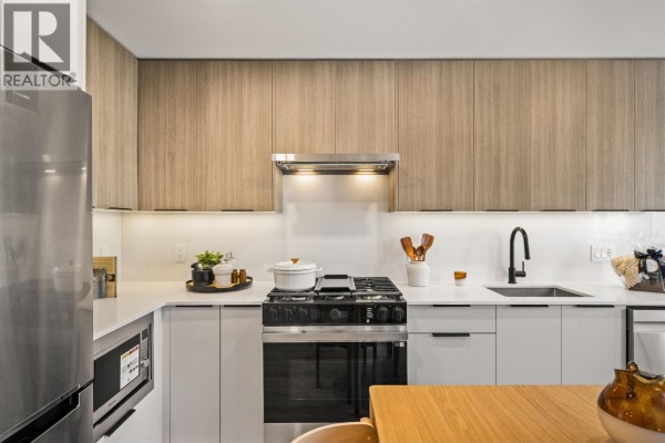 Close-up of kitchen with stainless steel stove, sink, and wooden cabinetry. - 306 111 Buller Street, Port Moody