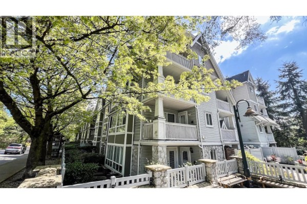 Building entrance with covered walkway, bushes, and stone pillars. - 306 1111 Lynn Valley Road, North Vancouver